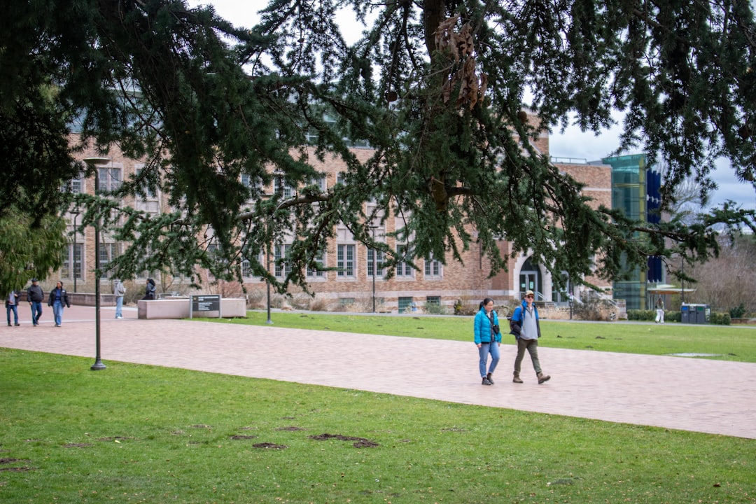 Students walk by a campus building under a tree.