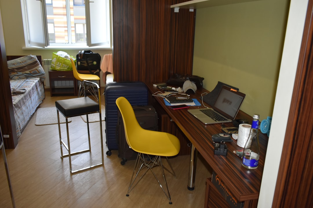 A cluttered room with a desk, chairs, and luggage.
