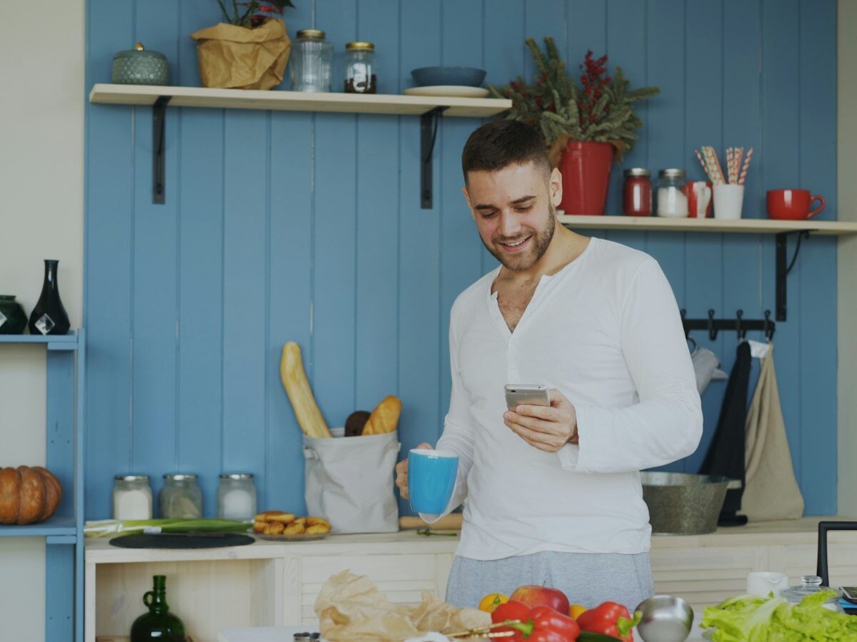 Jonge bewoner leest een verdachte mail op zijn telefoon in de keuken