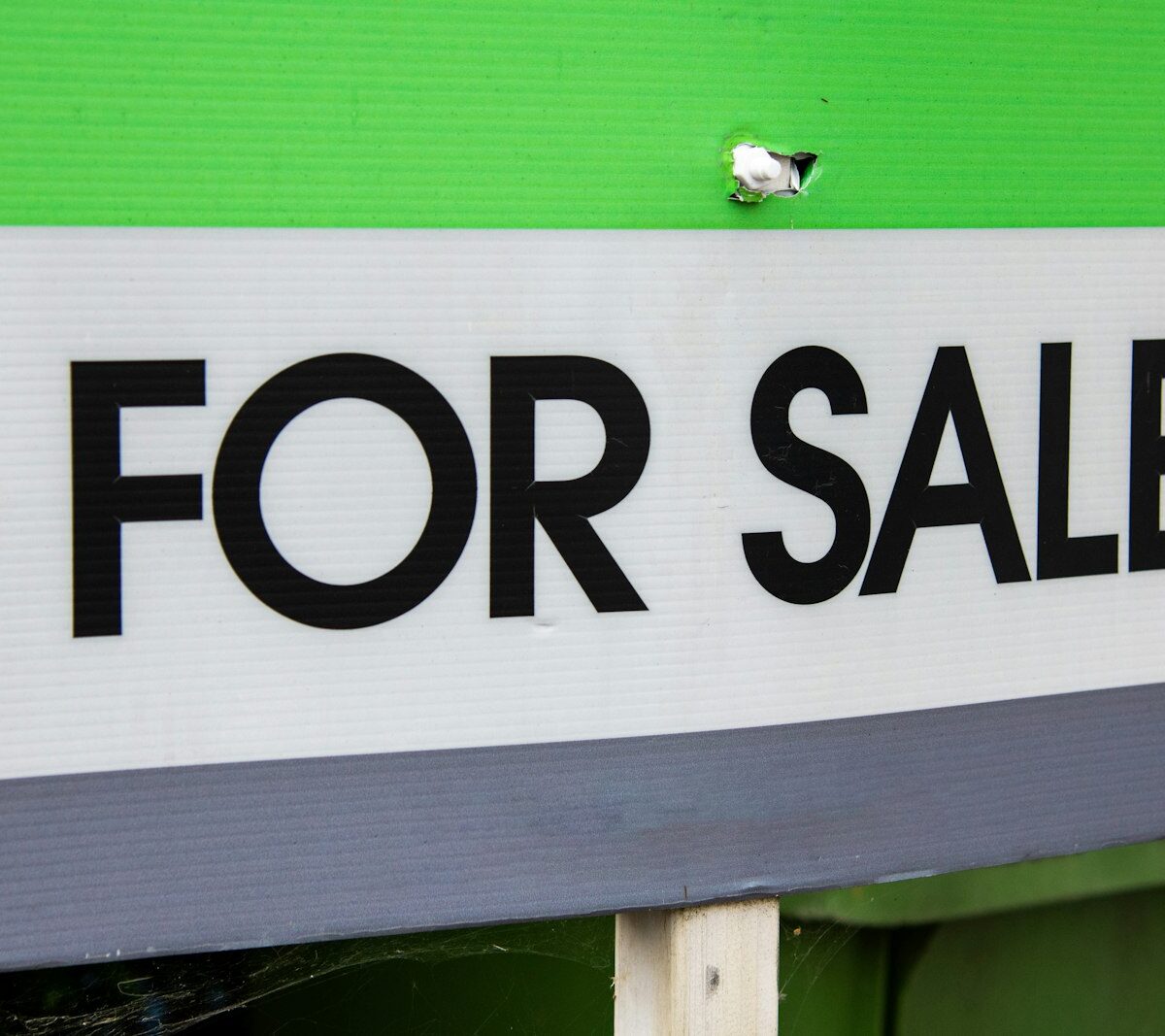 Jong stel staat voor de voordeur van een rijtjeshuis met een te koop-bord