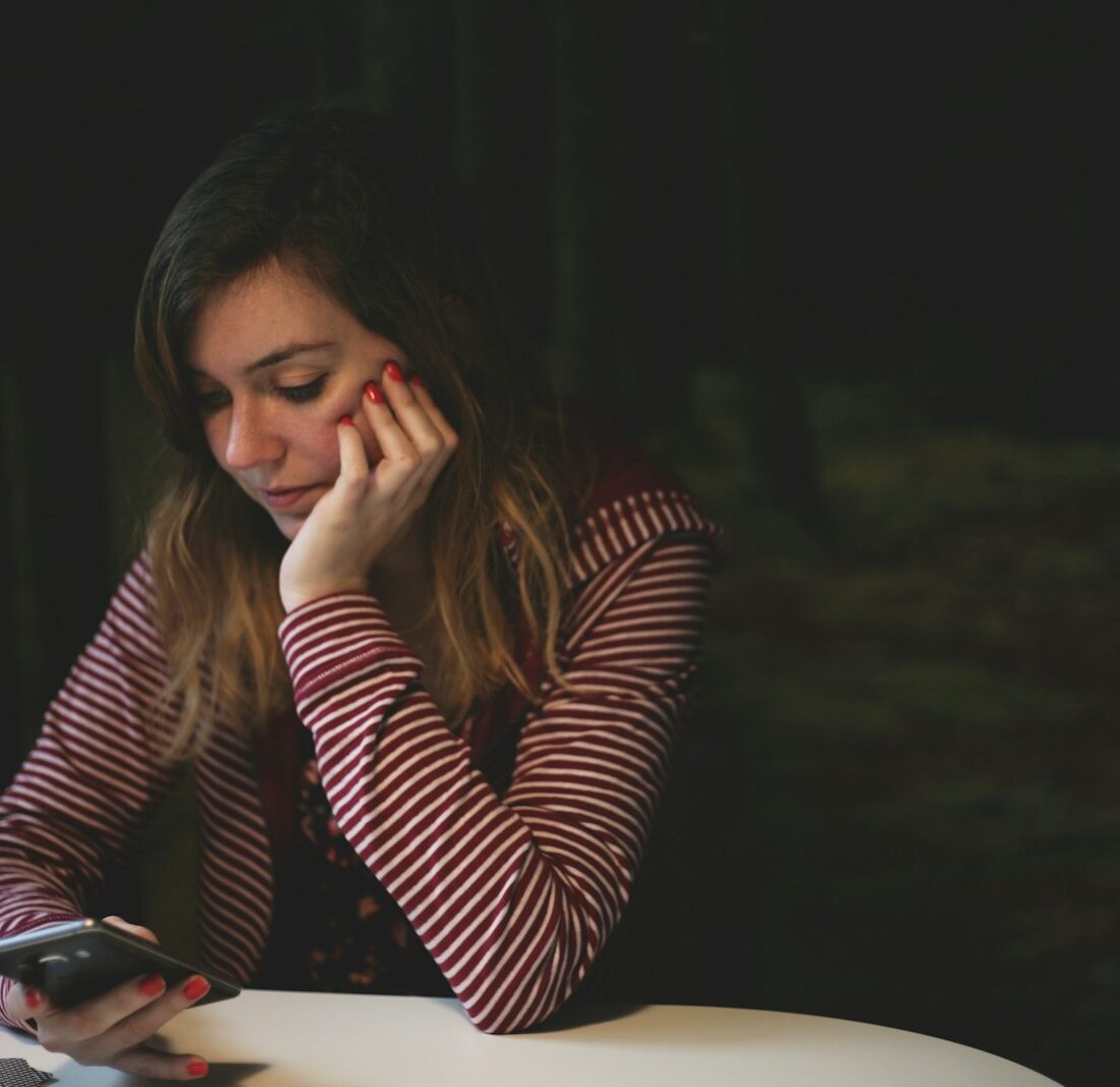 Jonge vrouw met verkoudheid op de bank met telefoon in de hand
